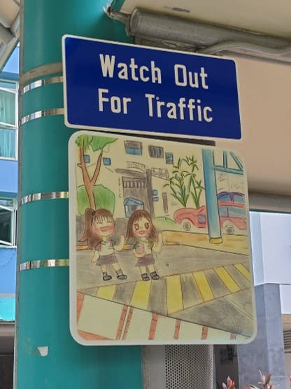 Student artwork promoting safe road crossing beneath a traffic sign.